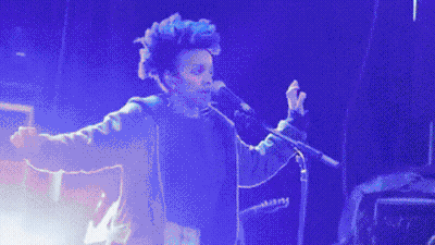 A Man Singing Into A Microphone While Another Man Plays A Bass Guitar GIF
