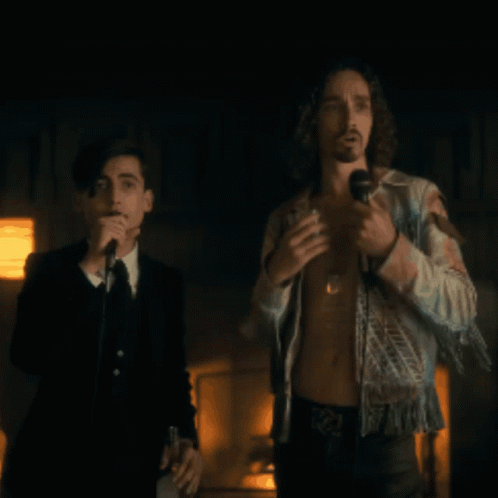 A Man Singing Into A Microphone While Another Man Stands Behind Him GIF