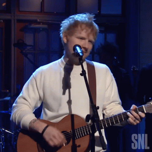 A Man Singing Into A Microphone While Holding A Guitar In Front Of A Snl Logo GIF