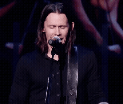 A Man Singing Into A Microphone While Playing A Guitar GIF
