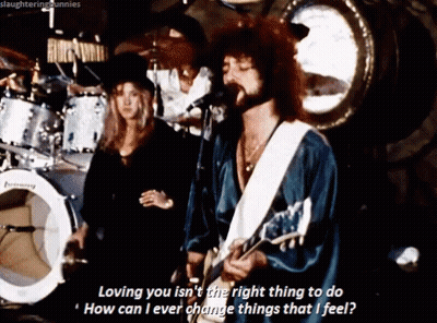 A Man Singing Into A Microphone While Playing A Guitar And A Woman Stands Behind Him GIF