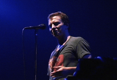 A Man Singing Into A Microphone While Wearing A Shirt That Says ' The Rolling Stones ' On It GIF