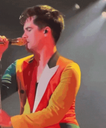 A Man Singing Into A Microphone With A Colorful Jacket On GIF