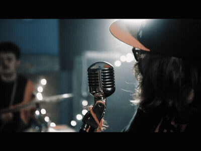 A Man Singing Into A Microphone With A Hat That Says La On It GIF