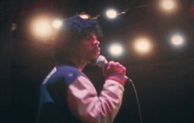 A Man Singing Into A Microphone With A Jacket That Has The Word Reebok On It GIF