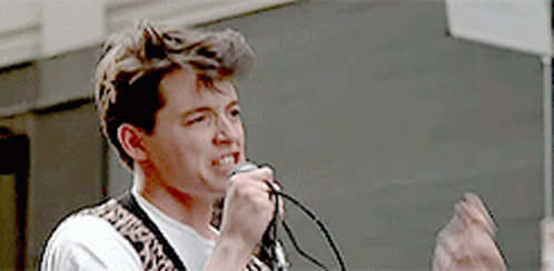 A Man Singing Into A Microphone With A Leopard Print Belt Around His Waist GIF