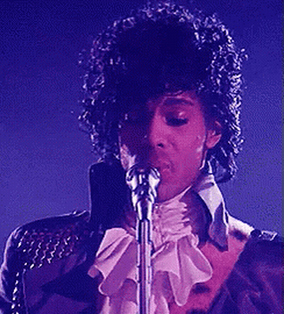 A Man Singing Into A Microphone With A Purple Background GIF