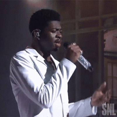 A Man Singing Into A Microphone With A Snl Logo In The Background GIF