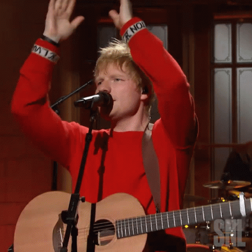 A Man Singing Into A Microphone With His Arms In The Air GIF