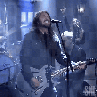 A Man Singing Into A Microphone With The Letters Snl Visible In The Background GIF