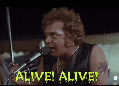 A Man Singing Into A Microphone With The Words Alive Alive Written On The Screen GIF