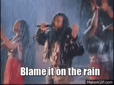 A Man Singing Into A Microphone With The Words Blame It On The Rain Above Him GIF