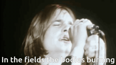 A Man Singing Into A Microphone With The Words In The Fields The Bodies Burning Above Him . GIF
