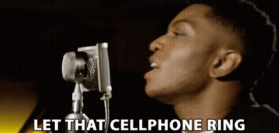 A Man Singing Into A Microphone With The Words Let That Cellphone Ring Behind Him GIF