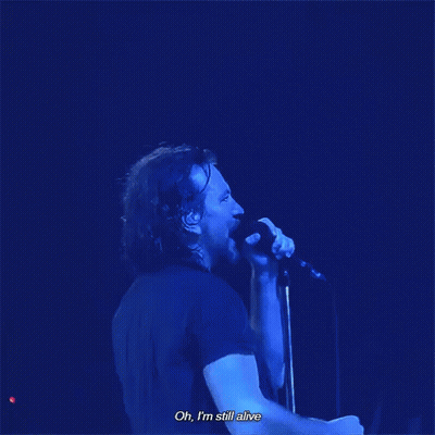 A Man Singing Into A Microphone With The Words Oh , I 'M Still Alive Below Him GIF