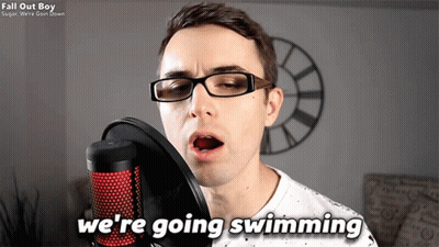 A Man Singing Into A Microphone With The Words " We 'Re Going Swimming " Next To Him GIF