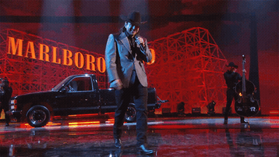 A Man Singing On Stage In Front Of A Sign That Says Marlboro GIF