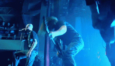 A Man Sings Into A Microphone While Another Man Holds A Guitar GIF