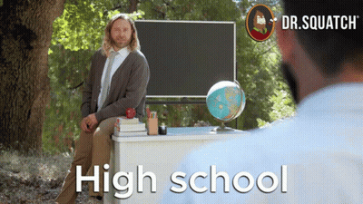 A Man Sits At A Desk In Front Of A Blackboard With The Words High School On It GIF