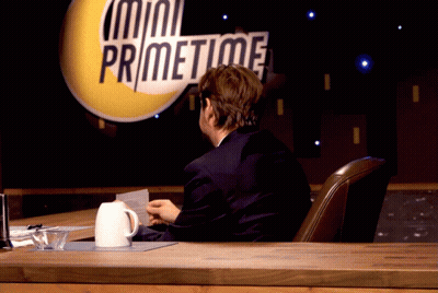 A Man Sits At A Desk In Front Of A Mini Primetime Sign GIF