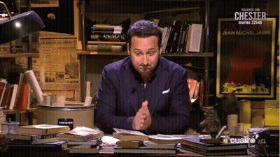 A Man Sits At A Desk In Front Of A Sign That Says Chester On It GIF