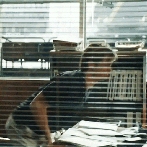 A Man Sits At A Desk In Front Of A Window GIF