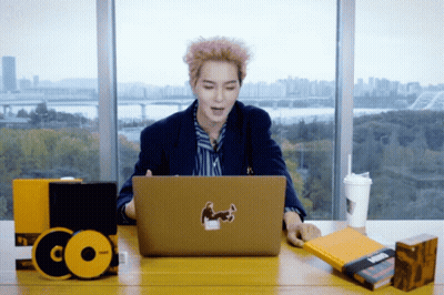 A Man Sits At A Desk Using A Laptop With A Sticker On It GIF