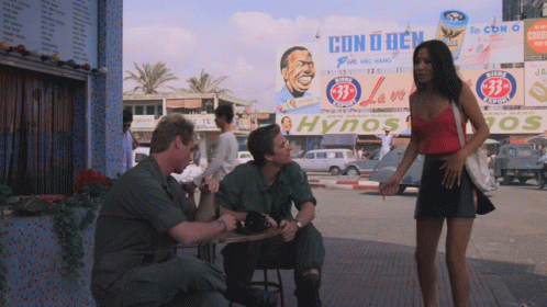 A Man Sits At A Table In Front Of A Billboard That Says Con U Bien GIF