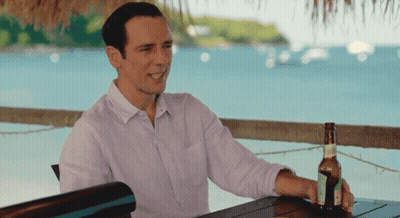 A Man Sits At A Table With A Bottle Of Beer In His Hand GIF
