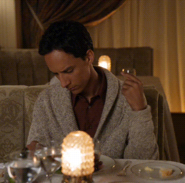 A Man Sits At A Table With A Glass Of Wine And A Candle GIF