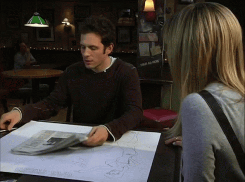 A Man Sits At A Table With A Newspaper And A Piece Of Paper That Says " Your Ad Here " GIF