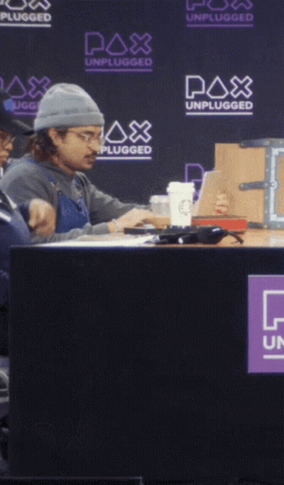 A Man Sits At A Table With A Watch Out Sign In Front Of Him GIF