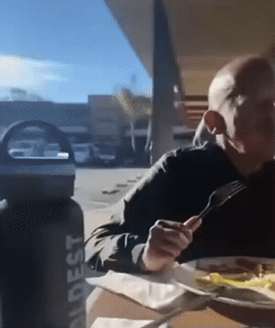 A Man Sits At A Table With A Water Bottle That Says ' Adest ' On It GIF