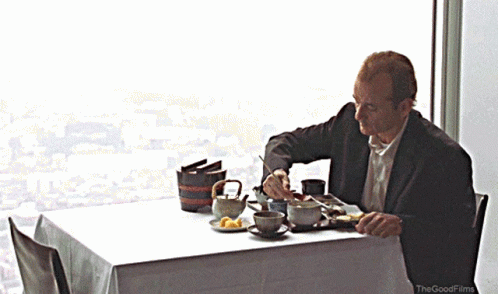 A Man Sits At A Table With A White Table Cloth And The Good Films Logo GIF