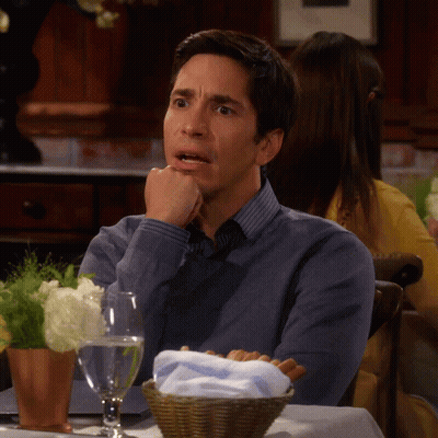 A Man Sits At A Table With His Hand On His Chin GIF