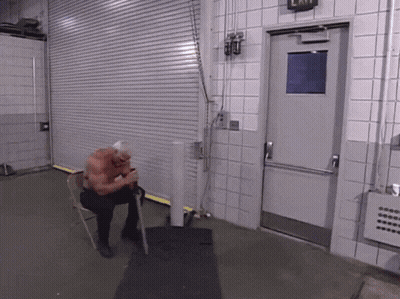 A Man Sits In A Chair In Front Of A Door That Has An Exit Sign On It GIF