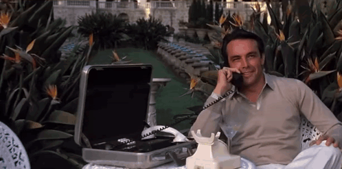 A Man Sits In A Chair Talking On A Phone GIF
