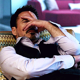 A Man Sits In A Chair With His Hand To His Face GIF
