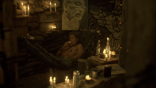 A Man Sits In A Dark Room With Candles And A Picture On The Wall GIF