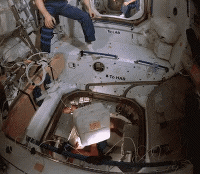 A Man Sits In A Space Station With A Sign That Says To Lab And To Hab GIF