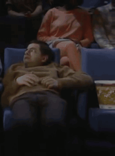 A Man Sits In A Theater With A Box Of Popcorn GIF