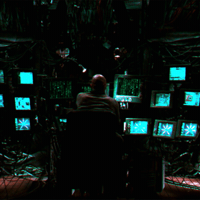 A Man Sits In Front Of A Bunch Of Computer Monitors Including One That Says ' Exit ' On It GIF