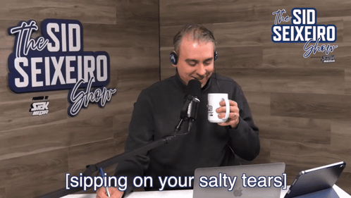 A Man Sits In Front Of A Microphone In Front Of A Sign That Says " The Sid Seixeiro Show " GIF