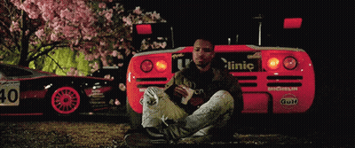 A Man Sits In Front Of A Red Car With The Number 40 On The Back GIF