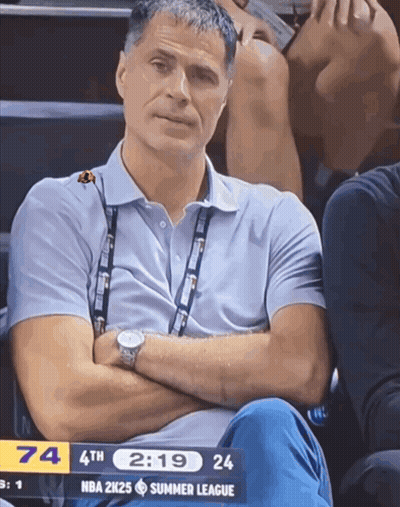 A Man Sits In The Stands With His Arms Crossed And A Nba 2K25 Summer League Scoreboard In The Background GIF
