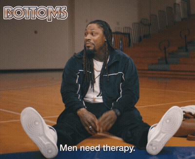 A Man Sits On A Basketball Court With The Words Men Need Therapy Above Him GIF
