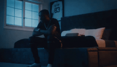 A Man Sits On A Bed In Front Of A Window With A Jersey On The Wall That Says 83 GIF