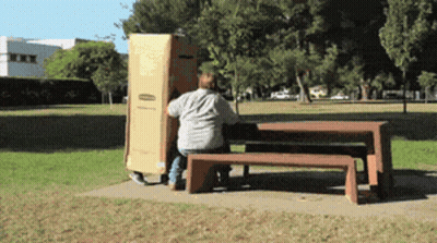 A Man Sits On A Bench In A Park While Carrying A Box GIF