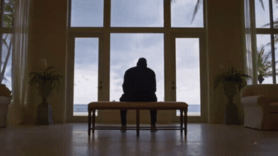 A Man Sits On A Bench In Front Of A Window Looking Out GIF