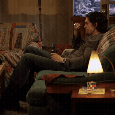 A Man Sits On A Couch Drinking A Beer GIF